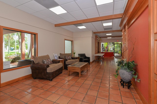 tiled living area with a wealth of natural light, a drop ceiling, and baseboards