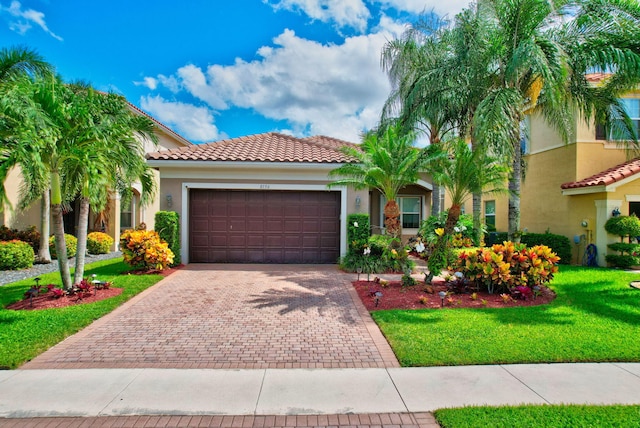 mediterranean / spanish home with decorative driveway, stucco siding, a front yard, a garage, and a tiled roof