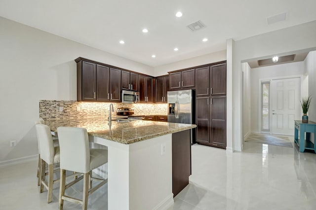 kitchen with light stone counters, stainless steel appliances, tasteful backsplash, visible vents, and a peninsula