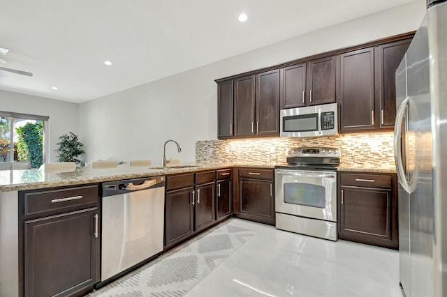 kitchen featuring dark brown cabinetry, tasteful backsplash, a peninsula, stainless steel appliances, and a sink