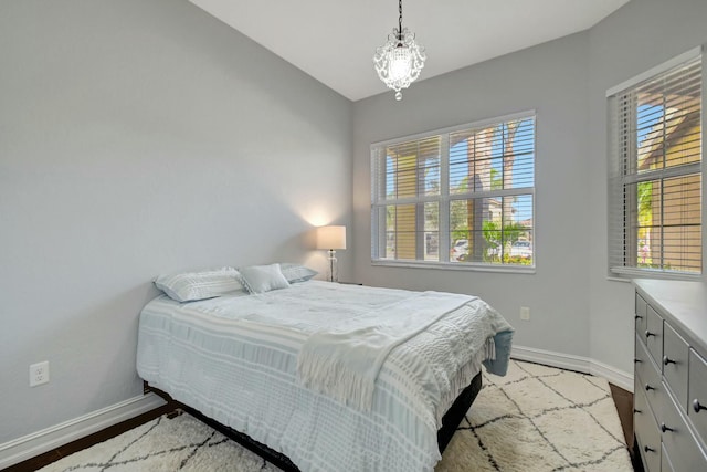 bedroom featuring a notable chandelier, vaulted ceiling, wood finished floors, and baseboards