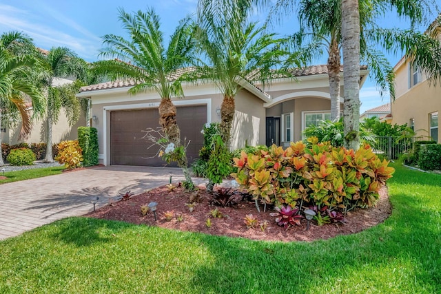 mediterranean / spanish house with a garage, a tile roof, decorative driveway, a front lawn, and stucco siding