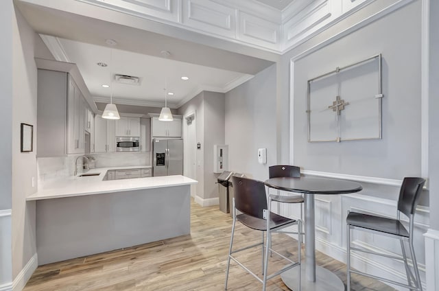 kitchen with light countertops, appliances with stainless steel finishes, ornamental molding, a sink, and light wood-type flooring