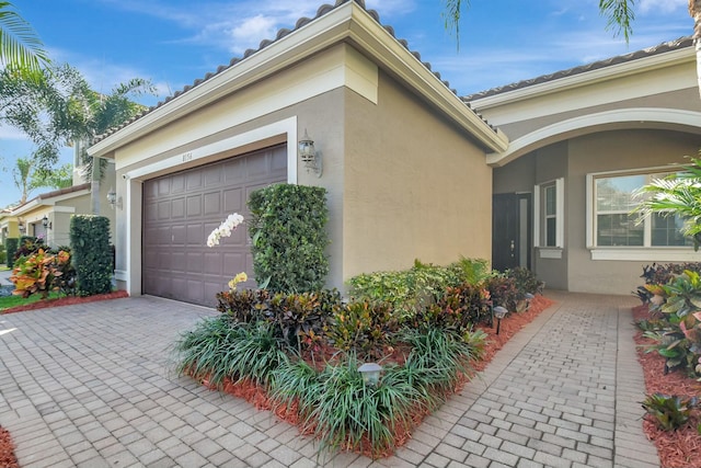 view of property exterior featuring an attached garage, decorative driveway, and stucco siding