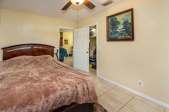 bedroom featuring a walk in closet, light tile patterned floors, visible vents, a ceiling fan, and baseboards