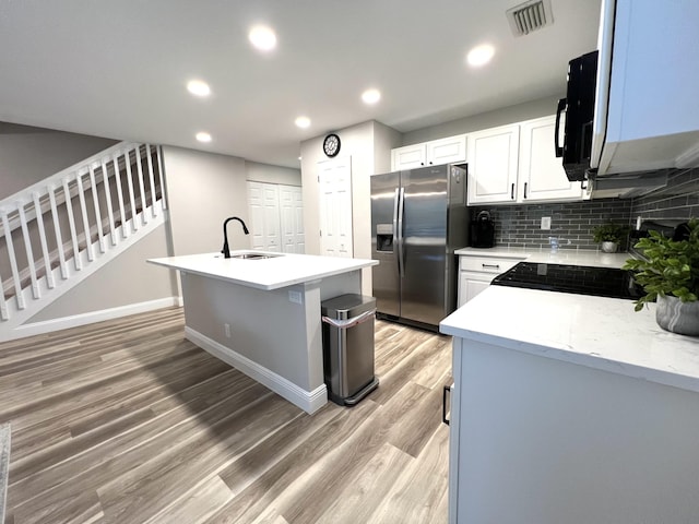 kitchen with light countertops, stainless steel fridge, a sink, and an island with sink