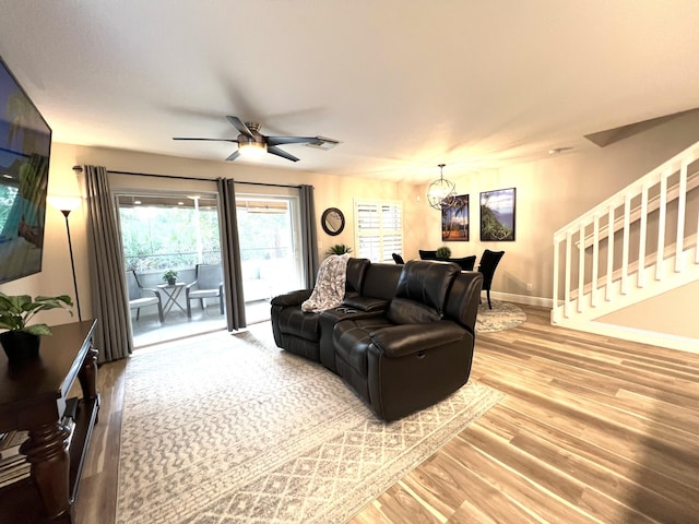 living room with stairs, visible vents, wood finished floors, baseboards, and ceiling fan with notable chandelier