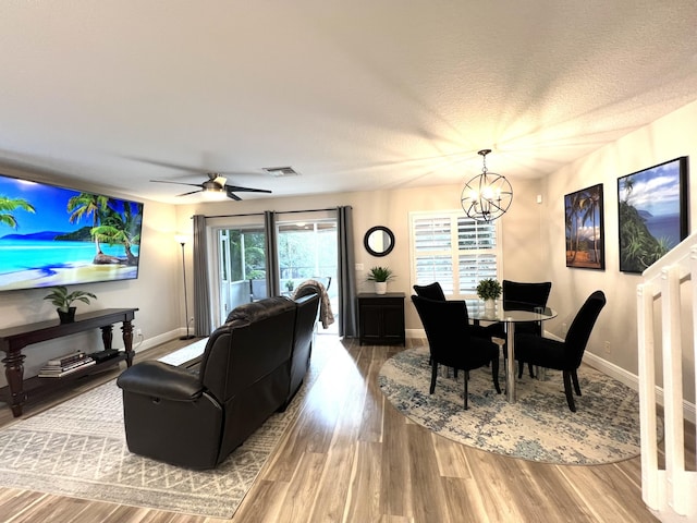 living area featuring baseboards, visible vents, wood finished floors, a textured ceiling, and ceiling fan with notable chandelier