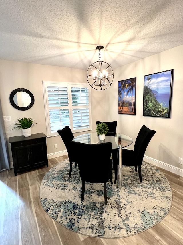 dining room featuring a chandelier, a textured ceiling, baseboards, and wood finished floors