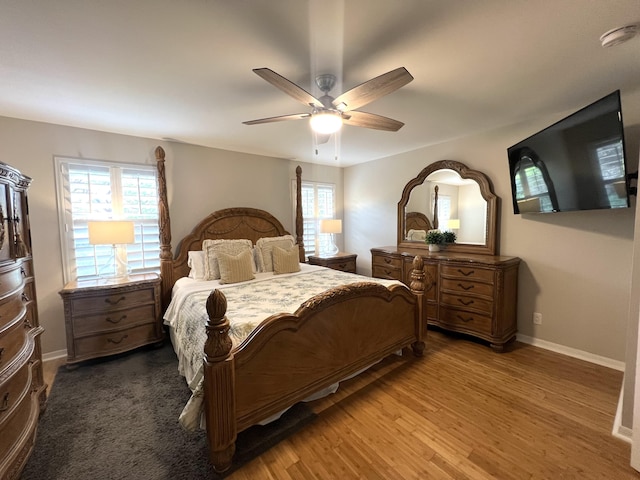 bedroom featuring ceiling fan, multiple windows, baseboards, and wood finished floors