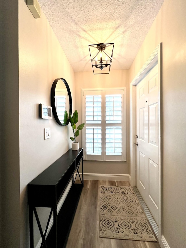 doorway with a textured ceiling, baseboards, and wood finished floors