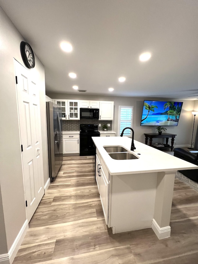 kitchen featuring a sink, white cabinets, light countertops, black appliances, and glass insert cabinets