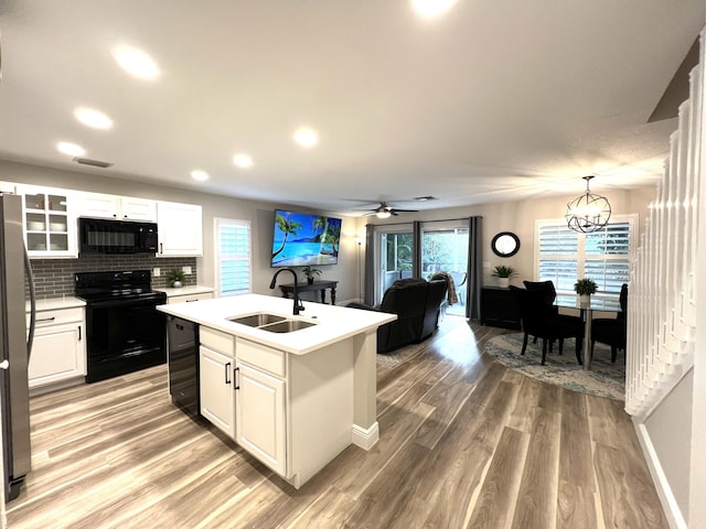 kitchen with a sink, light countertops, black appliances, an island with sink, and glass insert cabinets