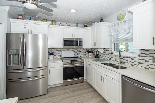 kitchen featuring light wood finished floors, stainless steel appliances, light countertops, white cabinetry, and a sink