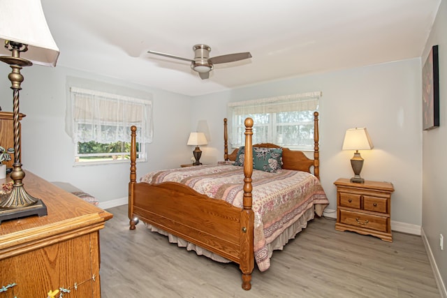 bedroom with a ceiling fan, multiple windows, light wood-style flooring, and baseboards