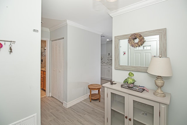 hall featuring light wood-style floors, visible vents, crown molding, and baseboards