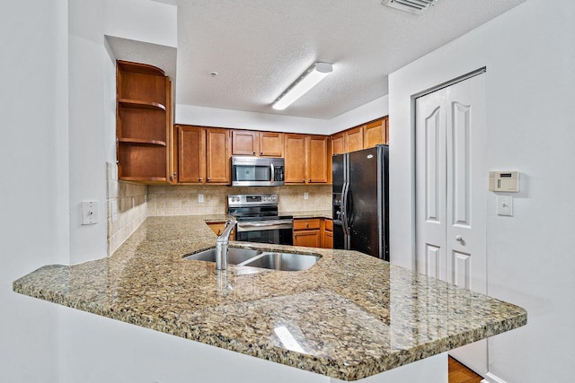 kitchen with a peninsula, appliances with stainless steel finishes, a sink, and light stone counters