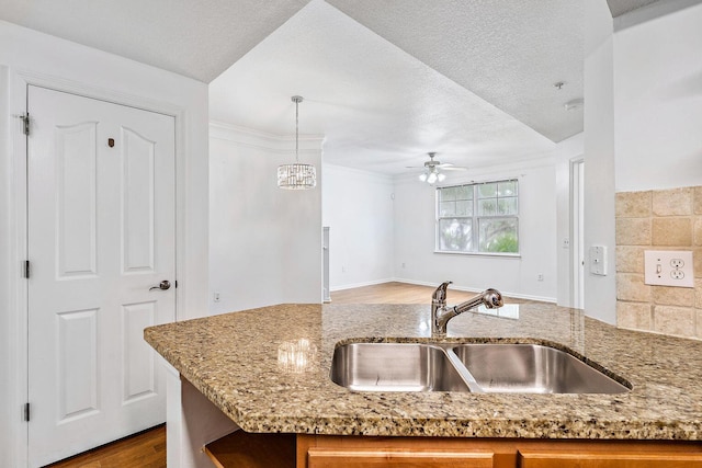 kitchen with open floor plan, wood finished floors, hanging light fixtures, light stone countertops, and a sink