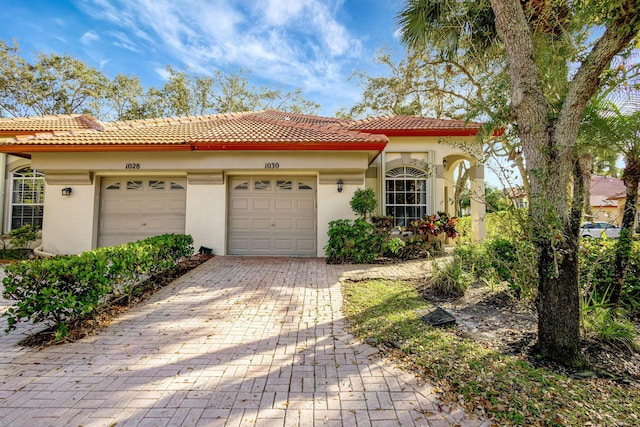 mediterranean / spanish-style home featuring decorative driveway, a tile roof, an attached garage, and stucco siding