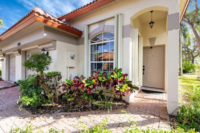 entrance to property featuring a garage, a tile roof, and stucco siding