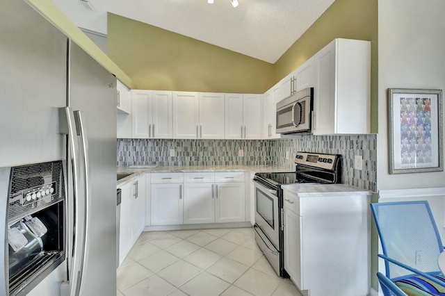 kitchen with lofted ceiling, light tile patterned flooring, stainless steel appliances, white cabinetry, and light countertops