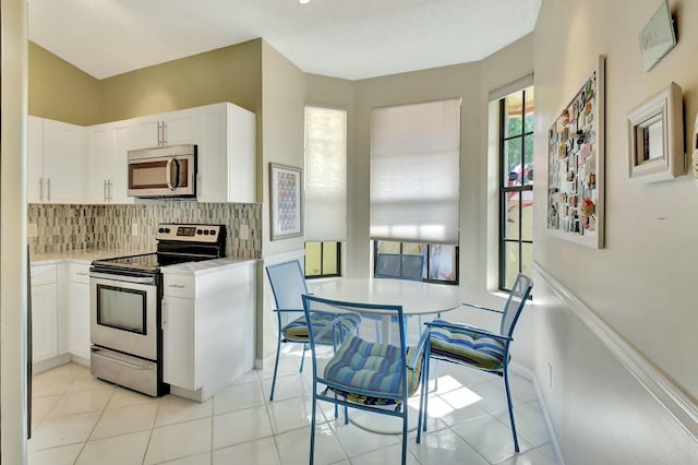 kitchen featuring light tile patterned flooring, stainless steel appliances, white cabinetry, light countertops, and backsplash