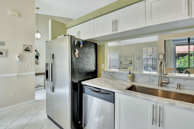 kitchen with light tile patterned floors, stainless steel appliances, a sink, white cabinetry, and decorative light fixtures