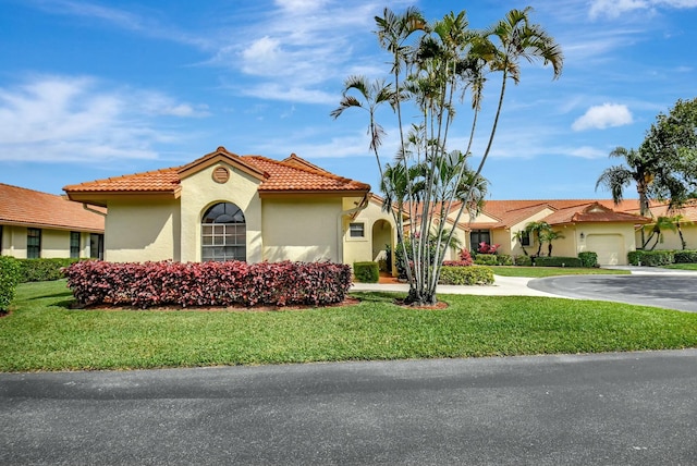 mediterranean / spanish-style house with driveway, a front lawn, a tile roof, and stucco siding