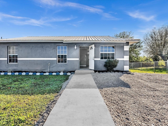 view of front of house featuring metal roof, a front lawn, fence, and stucco siding