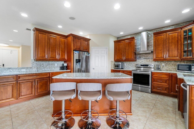 kitchen featuring a kitchen bar, appliances with stainless steel finishes, glass insert cabinets, a kitchen island, and wall chimney exhaust hood