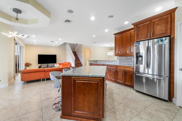 kitchen with light stone counters, visible vents, open floor plan, stainless steel fridge with ice dispenser, and tasteful backsplash