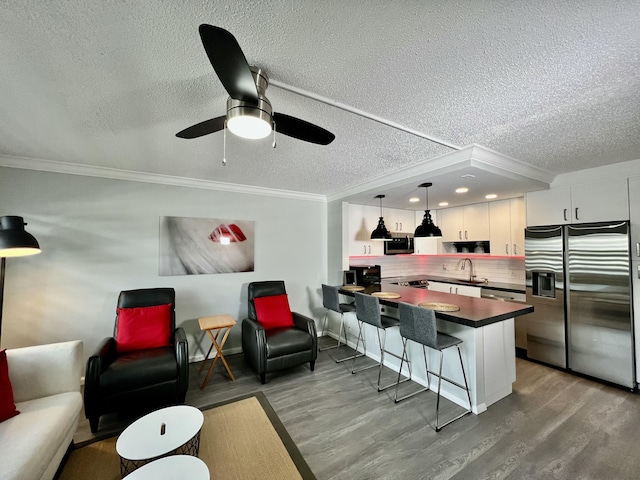 interior space featuring a breakfast bar area, a peninsula, white cabinets, dark countertops, and pendant lighting