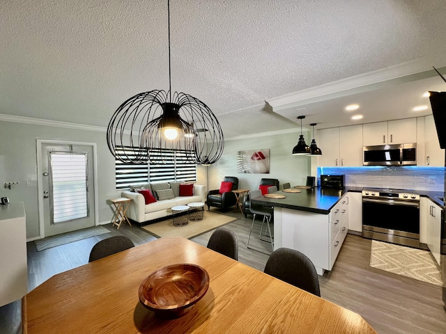 kitchen with stainless steel appliances, white cabinetry, light wood finished floors, dark countertops, and decorative light fixtures