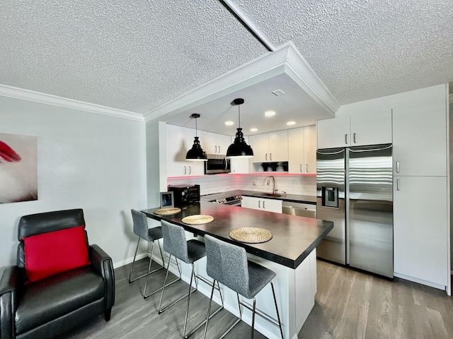 kitchen with dark countertops, a peninsula, pendant lighting, and stainless steel appliances