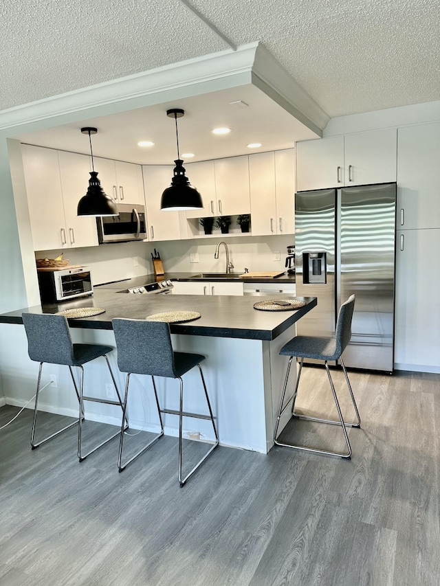 kitchen featuring pendant lighting, dark countertops, appliances with stainless steel finishes, wood finished floors, and a kitchen breakfast bar