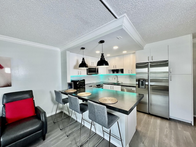 kitchen featuring stainless steel appliances, a peninsula, white cabinets, dark countertops, and pendant lighting