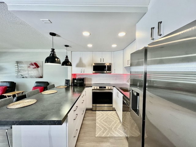 kitchen featuring white cabinets, dark countertops, a breakfast bar area, hanging light fixtures, and stainless steel appliances