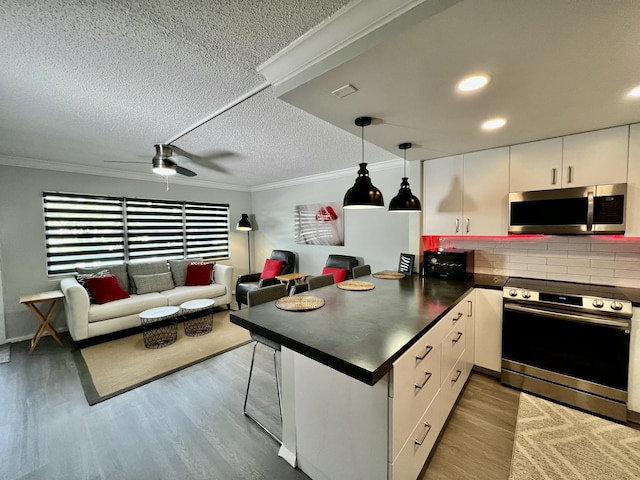 kitchen with stainless steel appliances, dark countertops, open floor plan, white cabinets, and a peninsula