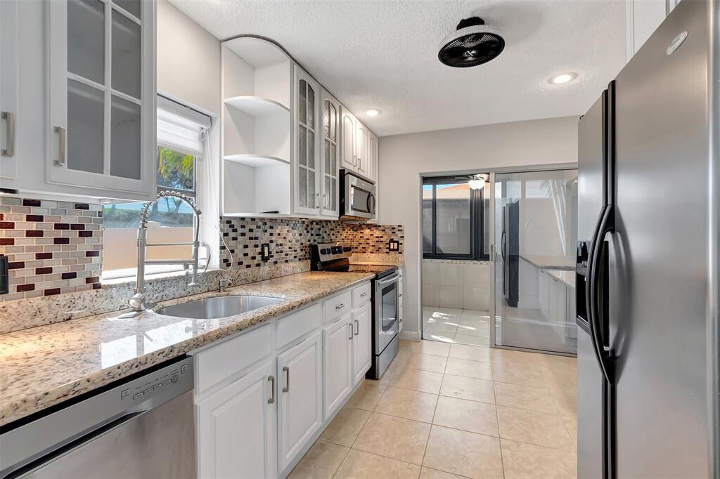 kitchen with open shelves, stainless steel appliances, glass insert cabinets, white cabinetry, and a sink