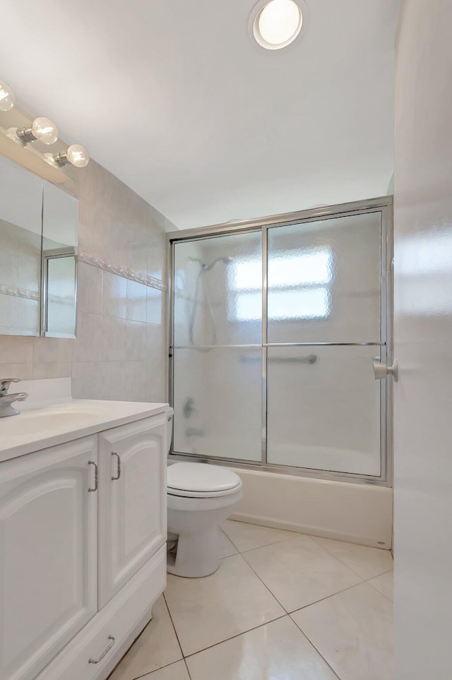 full bath featuring toilet, shower / bath combination with glass door, tile patterned flooring, vanity, and tile walls