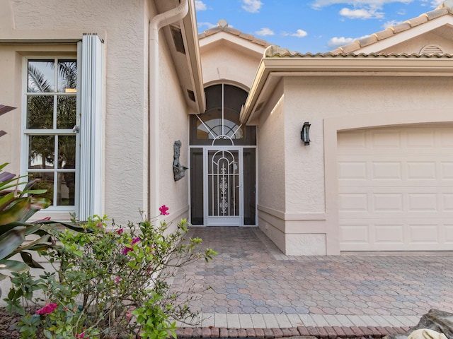 doorway to property with a tile roof, an attached garage, and stucco siding