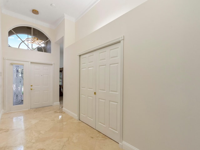 entryway featuring ornamental molding, marble finish floor, a towering ceiling, and baseboards