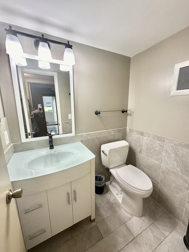 half bath with visible vents, toilet, a wainscoted wall, vanity, and tile walls