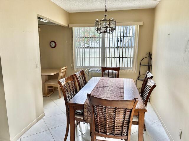 dining space with light tile patterned floors, baseboards, a chandelier, and a textured ceiling