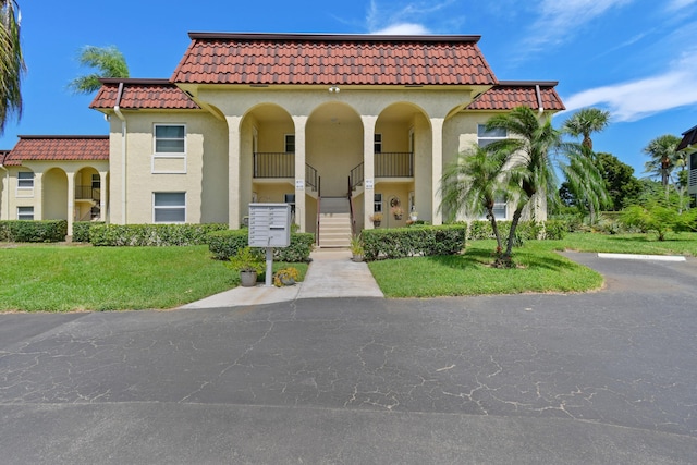 mediterranean / spanish house featuring a front lawn, stairway, a tile roof, and stucco siding