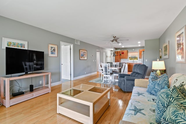 living room with ceiling fan, light wood finished floors, visible vents, and baseboards