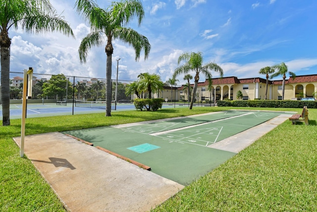 view of property's community with a tennis court, shuffleboard, fence, and a lawn