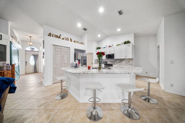 kitchen with visible vents, a breakfast bar, lofted ceiling, stainless steel appliances, and white cabinetry