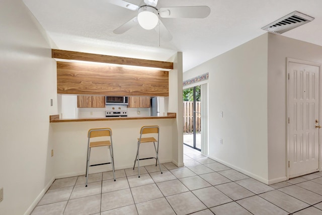 kitchen with visible vents, range with electric cooktop, a breakfast bar area, freestanding refrigerator, and light tile patterned flooring