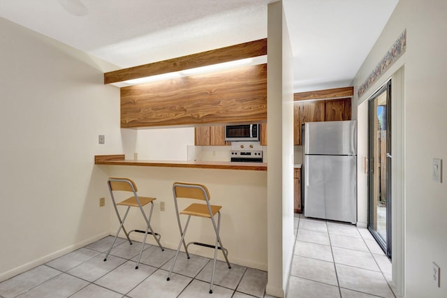 kitchen featuring light tile patterned floors, a breakfast bar, baseboards, appliances with stainless steel finishes, and brown cabinetry